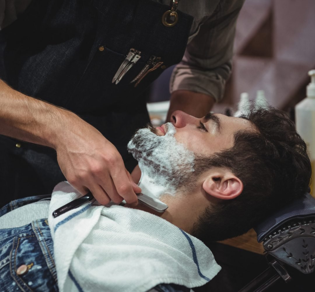 Man getting his beard shaved with razor in barber shop